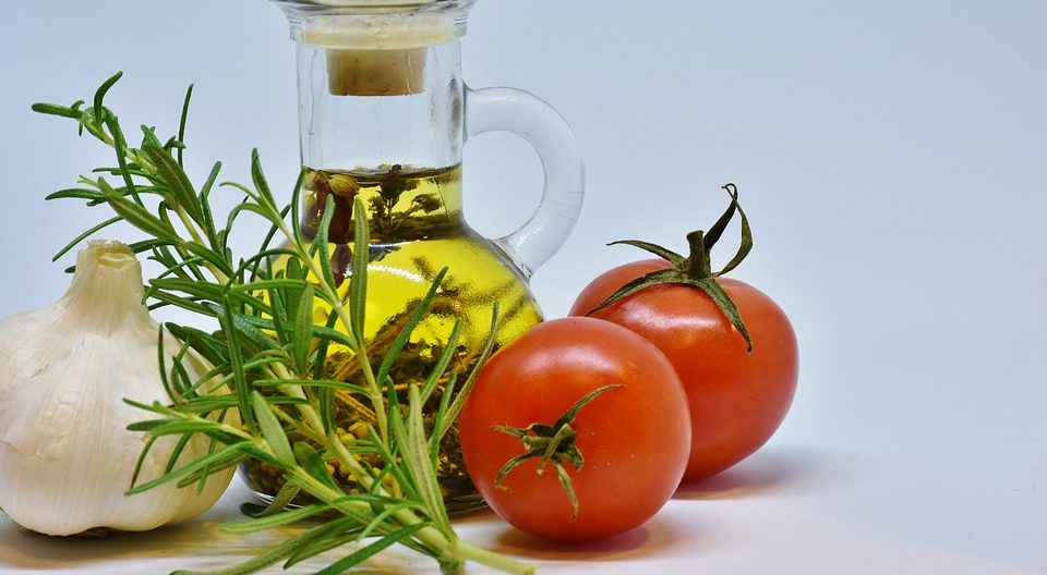 olive oil in a jar with a head of garlic, sprig of rosemary, and two plum tomatoes