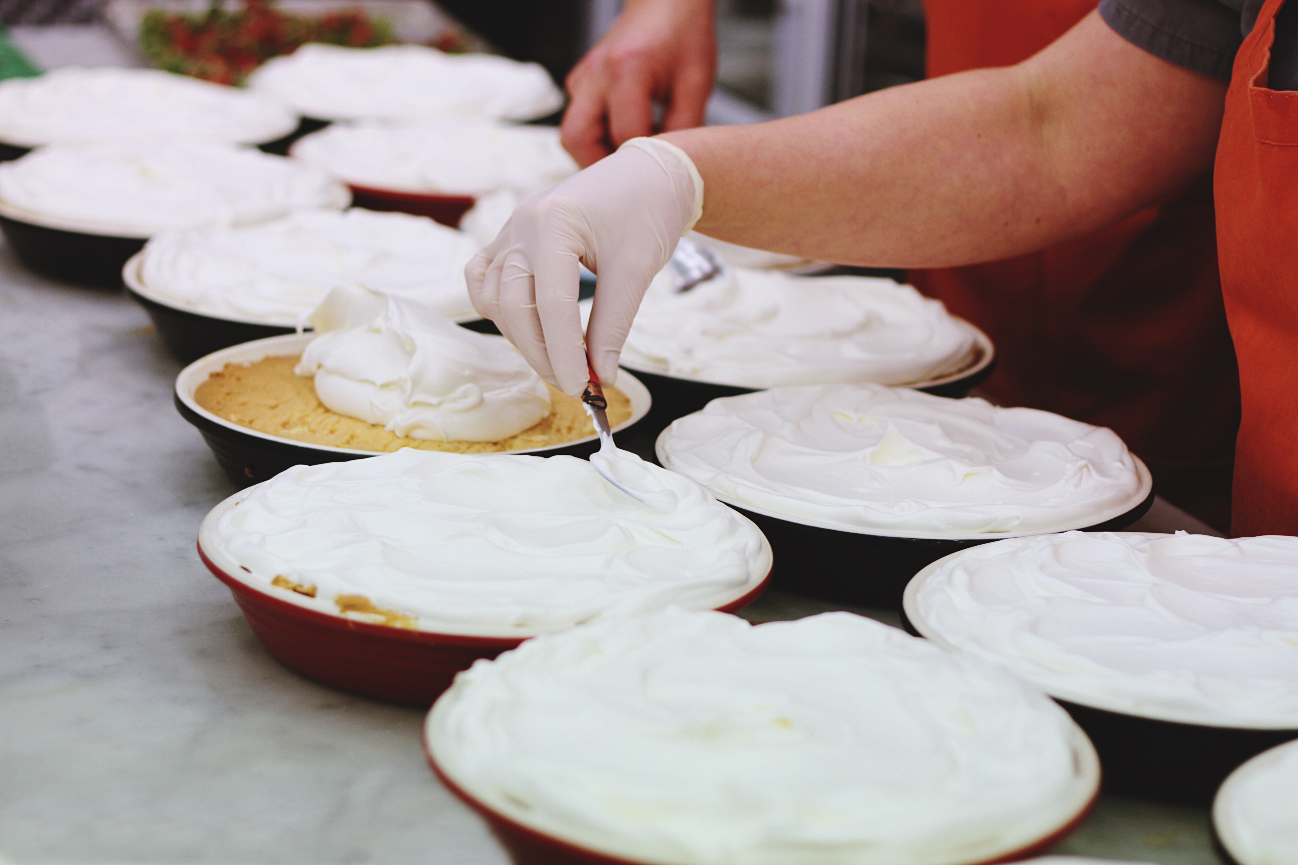 person wearing white latex gloves putting whipped cream on bowls