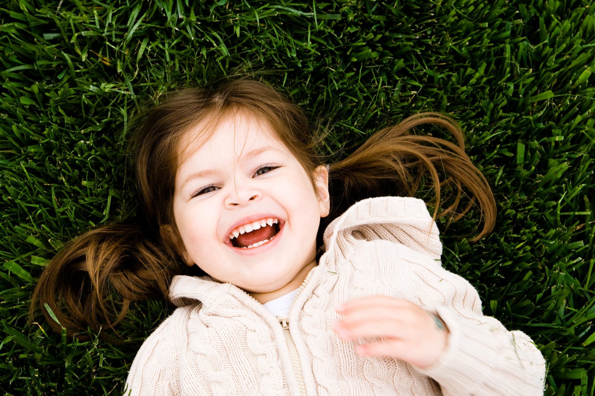 young girl smiling in grass with pigtails