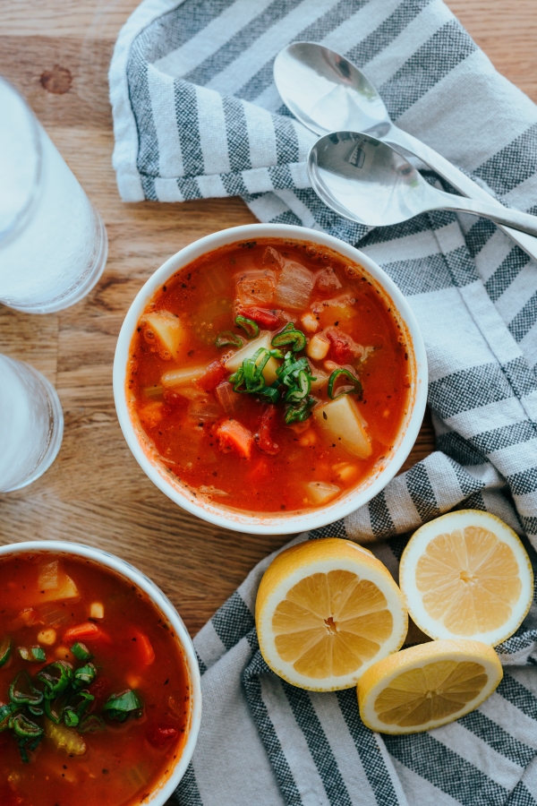 two bowls of minestrone soup on a wooden table near a towel and three lemons